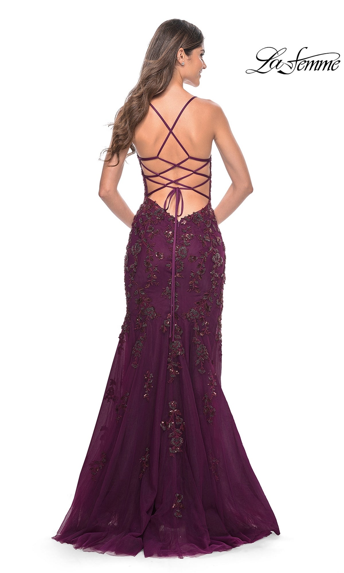 Woman in a La Femme Backless Long Lace Prom Dress 32307, deep purple with crisscross straps and floral embroidery, photographed from behind against a white background.